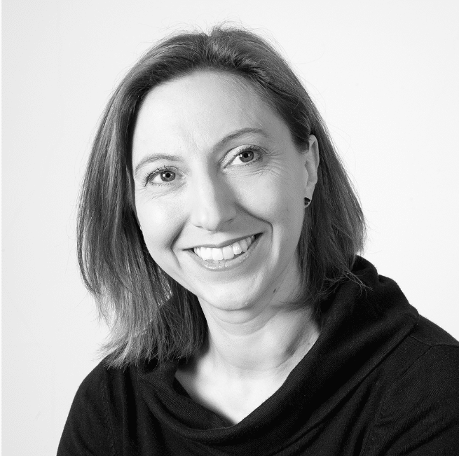 A grayscale portrait of a smiling woman, identified as Alexandra Stubbings, with shoulder-length hair. She's wearing a dark top and looking slightly to her left. The background is plain white, giving the photo a clean and professional appearance.